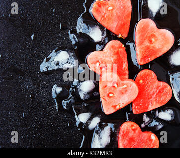 Watermelon coeurs avec des cubes de glace sur fond noir en noir pour la Saint-Valentin, selective focus, de l'espace pour le texte Banque D'Images