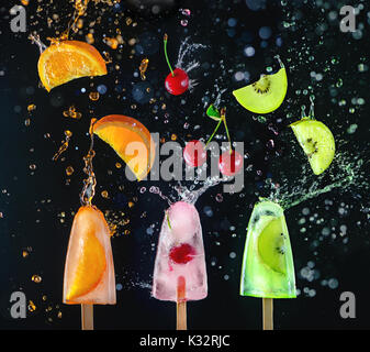 Les sucettes glacées avec des cerises fraîches, des tranches d'orange et le kiwi sur un fond sombre, dynamique tourné avec l'action, splash, gouttes et flou. La fonte des glaces Banque D'Images