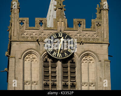 Horloge ensoleillée avec chiffres romains dorés et visage noir sur la tour de l'église en pierre Banque D'Images