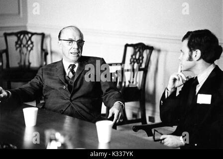 Portrait candide de l'Université Johns Hopkins, président Milton S. Eisenhower (à gauche) assis à une table et de parler à un chiffre non identifié au cours de la Milton S. Eisenhower 1971 Symposium, une série de conférences de l'Université John Hopkins, à Baltimore, Maryland, 1971. Banque D'Images