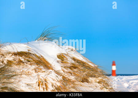 L'herbe des dunes couvertes de neige à l'hiver, ciel bleu et lointain phare, Warnemünde, Allemagne (copie espace) Banque D'Images