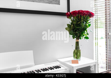 Bouquet de roses rouges sur le tableau blanc avec piano blanc en arrière-plan Banque D'Images