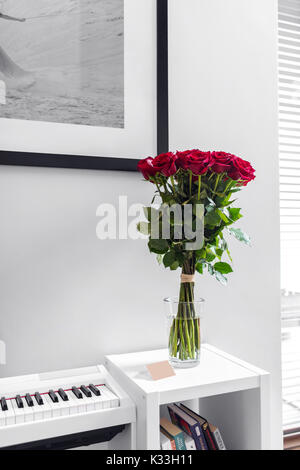 Bouquet de roses rouges sur le tableau blanc avec piano blanc en arrière-plan Banque D'Images