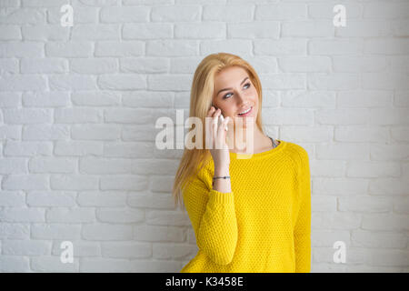 Une photo de jeune femme en pull jaune en conversation sur le téléphone mobile. Elle est à la recherche de contenu. Banque D'Images