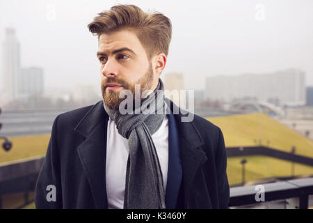 Une photo de jeune, beau homme portant un manteau et d'un châle. Il est à côté. Banque D'Images