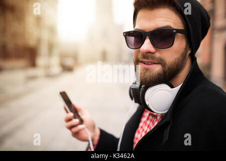 Une photo de l'homme jeune et branché avec un casque blanc sur son cou et d'un téléphone mobile dans sa main. Banque D'Images