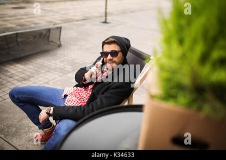 Une photo du jeune homme assis sur le transat et parler sur le mobile. Banque D'Images