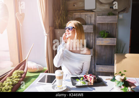 Une photo de jeune femme à lunettes assis à la table de café et de parler sur le mobile. Banque D'Images