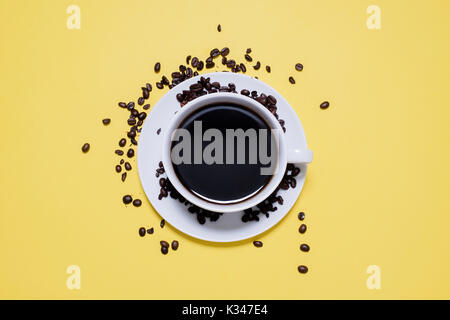 Tasse avec du café noir dans les grains de café renversé isolé sur un fond jaune lumineux Banque D'Images