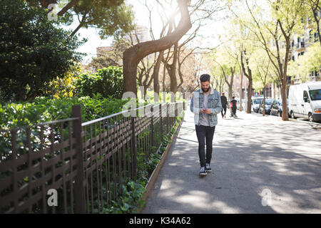 Une photo de jeune homme marchant sur le trottoir et regardant le mobile. Banque D'Images