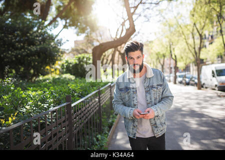 Une photo de jeune homme debout sur le trottoir avec un téléphone mobile dans ses mains. Banque D'Images