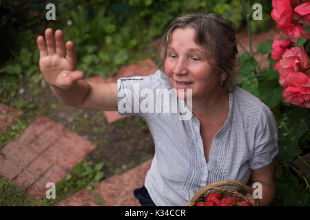 Cheerful mature femme est assise dans le jardin et forme à des amis Banque D'Images