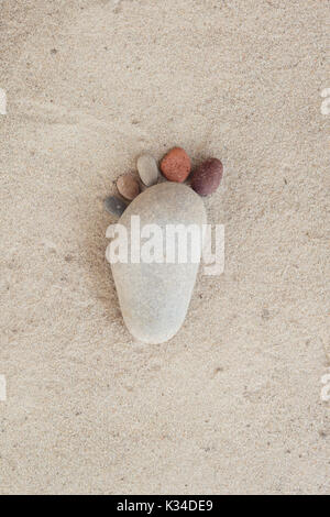 Groupe des pierres sur le sable de la création de forme d'un pied dans l'arrière-plan blanc isolé. Banque D'Images