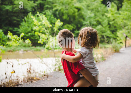 Un petit garçon est titulaire d'une petite fille sur un chemin bordé d'arbres. Banque D'Images