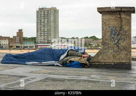 Homme endormi dans un sac de couchage sur un toit en face de la plage, dans la station balnéaire de Margate, Kent. Banque D'Images