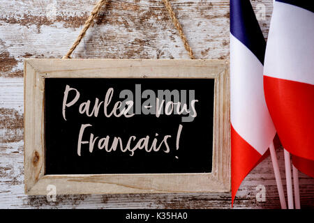 Un tableau en bois avec la question parlez-vous francais ? Parlez-vous français ? Écrit en français, et quelques drapeaux de la France contre la rouille Banque D'Images