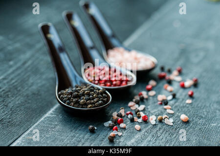 Portrait de trois cuillères à soupe de sel rose, noir et de poivre rose foncé sur fond de bois Banque D'Images