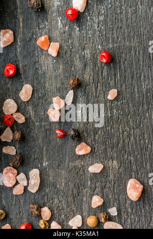 Close up de grains de sel de l'himalaya rose mélangé avec du poivre rose et rouge sur la surface en bois foncé Banque D'Images