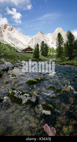 cooling down feet in the cold mountain river with the view to the mountain hut and alps in the back Banque D'Images