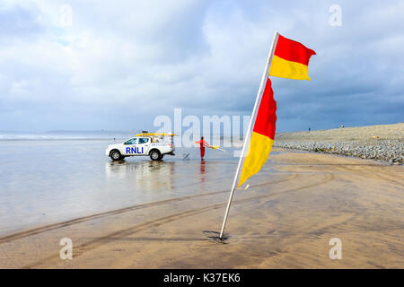 Un indicateur d'alerte rouge et jaune et sauveteur RNLI avec véhicule sur la plage de sable à Westward Ho ! À marée basse sous un ciel couvert et venteux jour d'été Banque D'Images