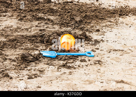 Seau en plastique bleu et orange et chat couché abandonnés sur la plage de sable à Westward Ho, Devon, UK Banque D'Images