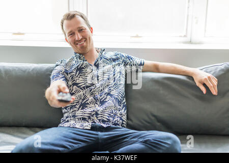 Accueil, de la technologie et de l'entretainment concept - smiling man with tv remote control à la maison Banque D'Images