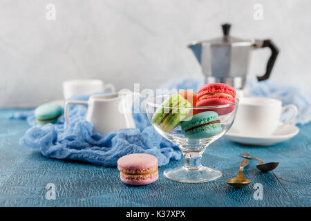 Le Français classique du maquereau colorée cookies en vase en verre, des tasses pour le café et le métal cafetière sur fond bleu Banque D'Images