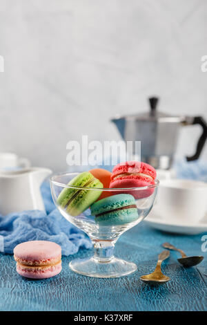 Le Français classique du maquereau colorée cookies en vase en verre, des tasses pour le café et le métal cafetière sur fond bleu Banque D'Images