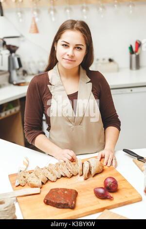 Jeune femme prépare un peu de nourriture dans la cuisine. Elle couper un pain. Banque D'Images