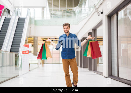 Une photo de jeune homme debout au milieu de la galerie marchande avec les sacs dans ses mains. Banque D'Images