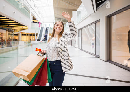 Une photo de jeune femme woman holding shopping bags and waving goodbye. Banque D'Images