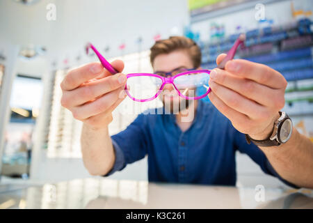 Une photo de jeunes, smiling man holding lunettes roses. Banque D'Images