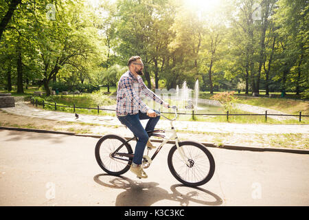 Portrait de côté happy man riding bike through park Banque D'Images