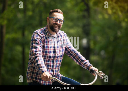 Face portrait of young smiling man riding bike at park Banque D'Images