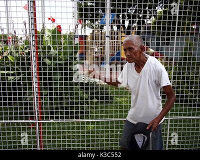 MARIKINA CITY, PHILIPPINES - le 28 août 2017 : Un vieil homme se tient à l'extérieur d'une aire de jeux pour enfants et tient à sa clôture en acier. Banque D'Images