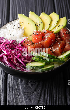 Bol de riz avec du thon poke, concombre, chou rouge et avocat, close-up sur la table. vertical Banque D'Images