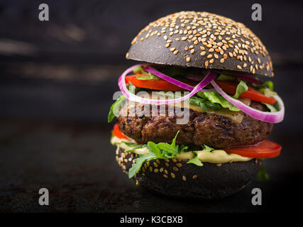 Big sandwich noir - noir avec hamburger burger de boeuf juteux, fromage, tomate et oignon rouge sur fond noir Banque D'Images