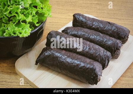 La cuisine japonaise traditionnelle, le riz japonais non tranché Maki Sushi Roll avec Nori Seaweed on Cutting Board servi avec chêne vert. Banque D'Images