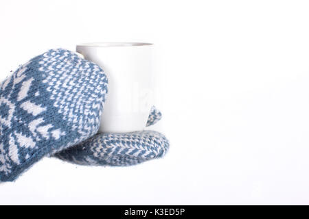 Les mains dans une paire de bleu et blanc hiver tricot mitaines tenant une tasse de café chaud, thé ou chocolat chaud Banque D'Images