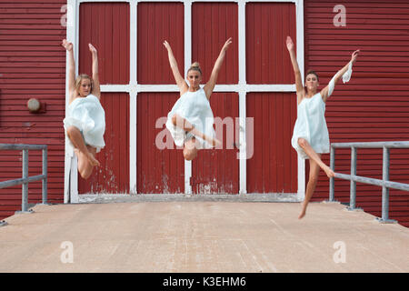 Trois sœurs de robes blanc à l'extérieur danse grange rouge aux beaux jours. Banque D'Images