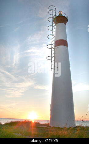 Un grand phare avec bandes rouges se trouve sur un rivage au coucher du soleil Banque D'Images