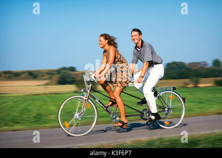 Jeune couple sur un tandem, femme va à l'avant Banque D'Images