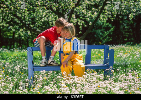 Fille et garçon assis sur un banc dans le jardin et Whisper Banque D'Images