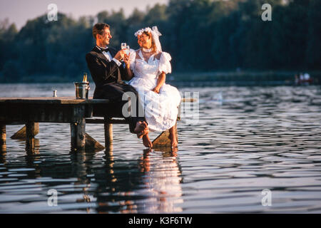 Wedding couple est assis sur un pont et de verre de champagne dans la main Banque D'Images