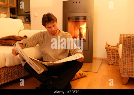 L'homme lit journal devant la cheminée du four Banque D'Images