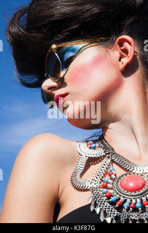 Portrait de la jeune femme adulte avec des lunettes de soleil à maquillage lourd et un grand collier Banque D'Images