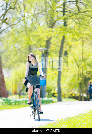 Vue Portrait of Girl sur location portant sur noir robe courte. Jeune femme heureuse équitation le long de la route sur vert printemps parc extérieur. Jeune fille sportive ri Banque D'Images