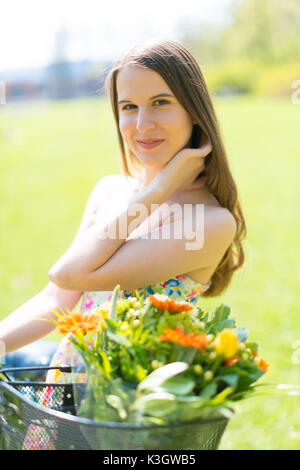 Portrait de jeune belle femme aux cheveux longs en parc d'été. A côté d'un vélo avec un panier de fleurs Banque D'Images