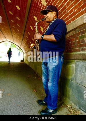 Saxophoniste dans l'ombre fraîche de la grauwacke Arch, Central Park, Manhattan, New York, NY, USA Banque D'Images