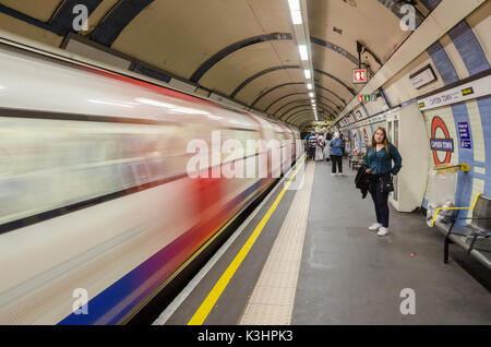 Une dame se tient et attend sur la plate-forme à la station de métro Camden Town comme un train à grande vitesse depuis les courses et est considéré comme un flou. Banque D'Images